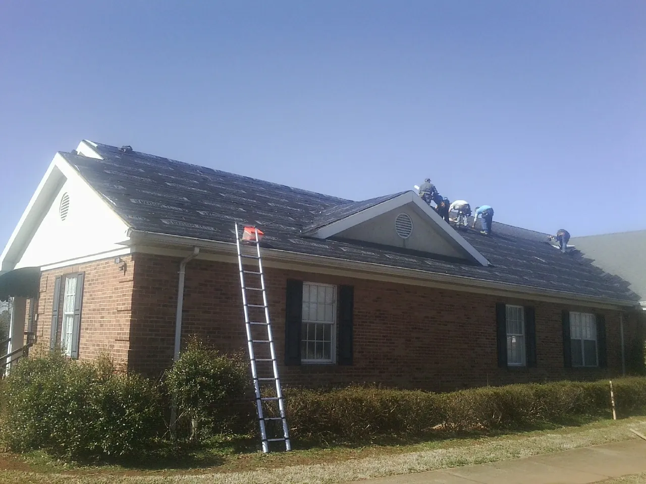 Crew tearing shingles off a brick ranch roof with a ladder set — Metal Roof Repair work by our crew in Fleischmanns