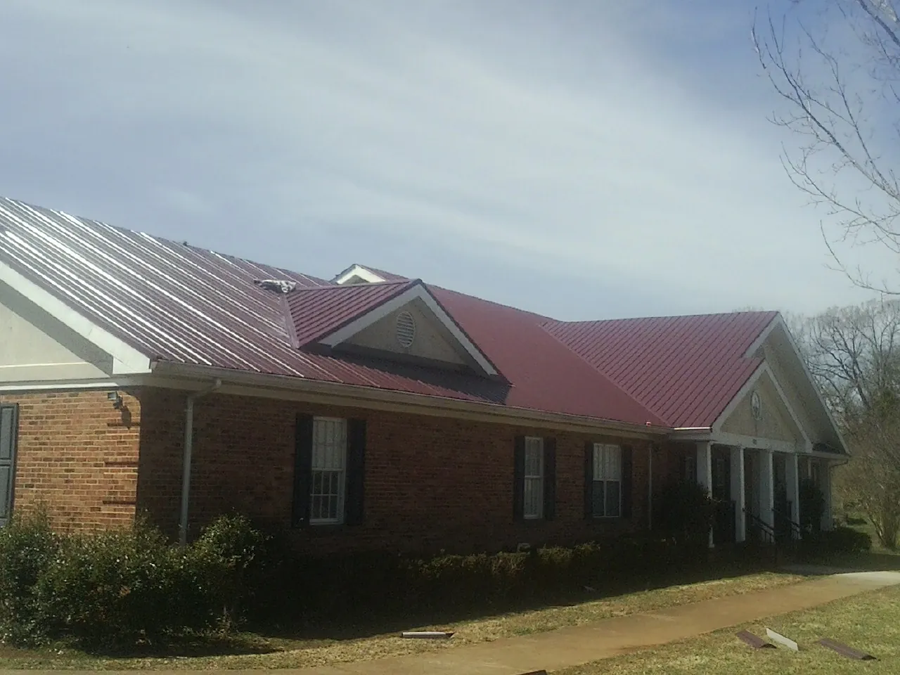 Red metal roof with gabled entries on a long brick building, from a Hail Damage Roof Repair job in Fleischmanns