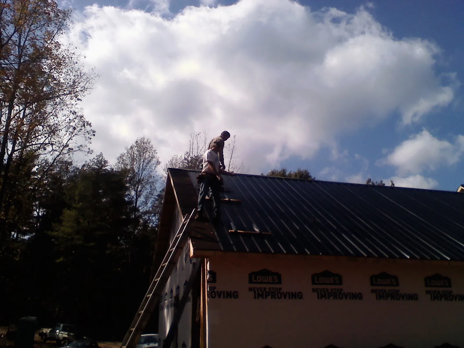 Roofer fastening dark metal panels high against a cloudy sky, from a Roof Inspection job in Fleischmanns
